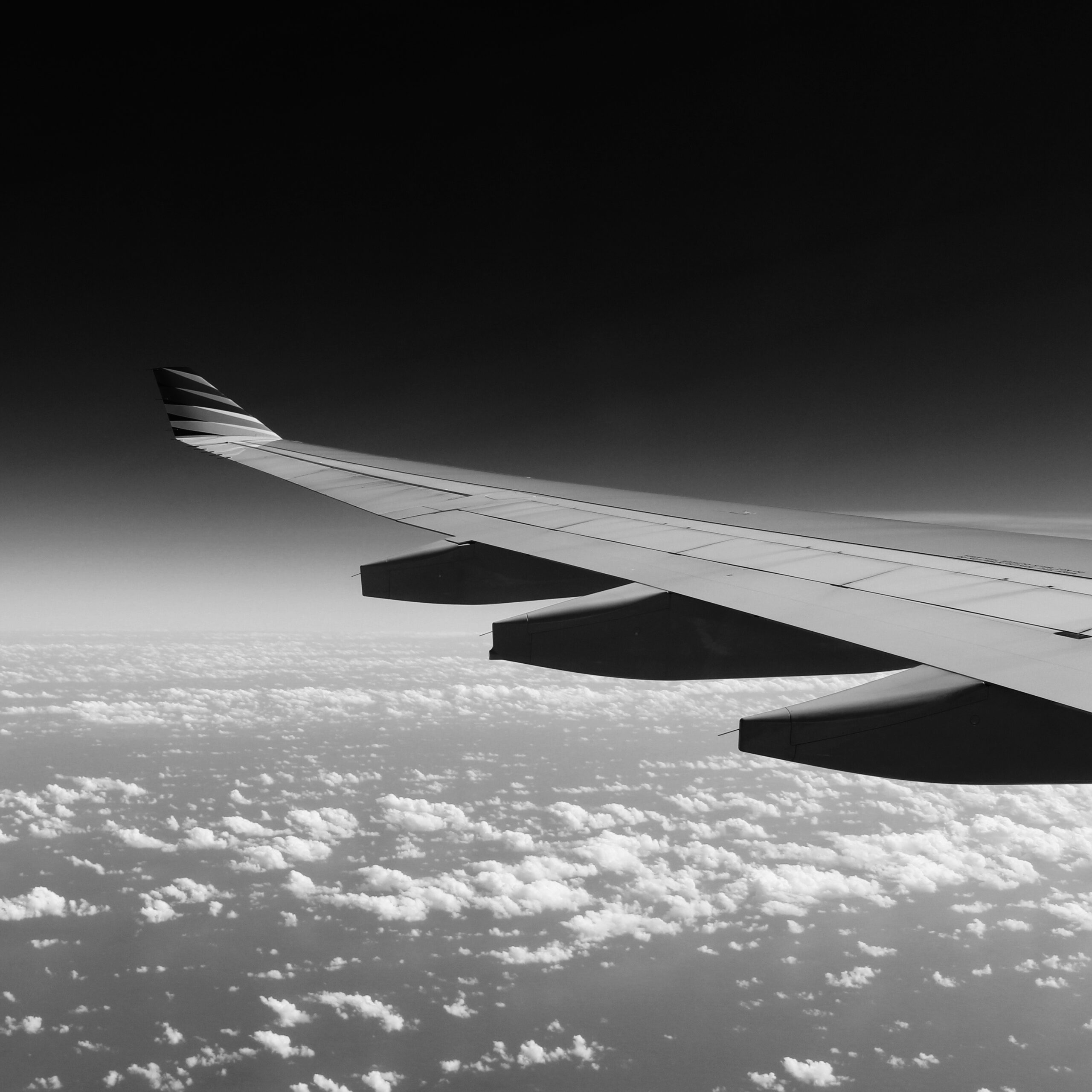 This is a black & white photo of the wing of a plane as it is flying.