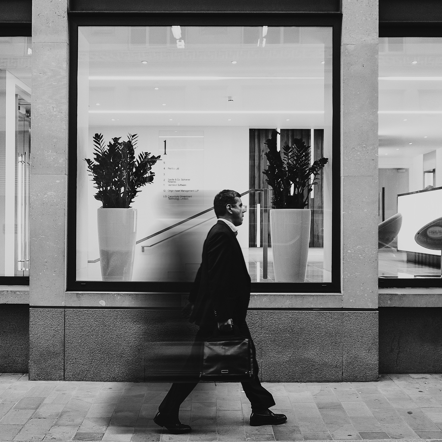 This is a black & white photo of a business man rushing down the street.